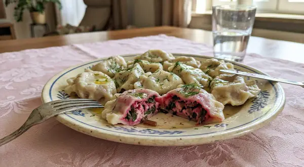 Pyszne pierogi z farszem na pierogi ruskie Magdy Gessler, polane masłem i posypane koperkiem. Jedna pierożka przekrojona, ukazująca bogate wnętrze.