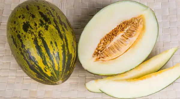 Un intero melone di Borgogna, tagliato a metà e a fette, mostra la sua polpa chiara e i semi dorati.