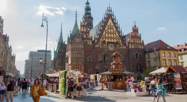 Rynek we Wrocławiu tętni życiem, oferując liczne wrocławskie atrakcje turystyczne. Ludzie spacerują wśród kramów i zabytkowej architektury.