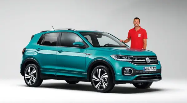 Mężczyzna w czerwonej koszulce stoi obok turkusowego Volkswagena T-Cross, który przekracza wymiary miejskiego auta.