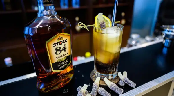 Butelka brandy Stock 84 i drink z cytryną, słomką i żelkami w kształcie butelek.
