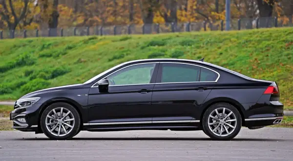 Elegancki, czarny sedan z chromowanymi detalami stoi na tle jesiennego krajobrazu.