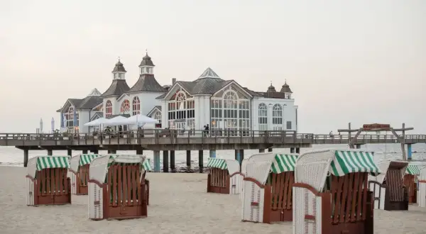 Plaża w Stralsundzie w Niemczech z charakterystycznymi koszami plażowymi i molo z białą budowlą.