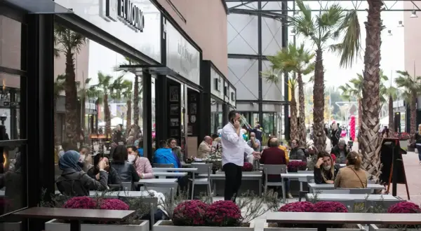 Gente disfrutando en los restaurantes de la torre outlet, rodeados de palmeras y flores.