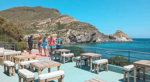 Terraza del cala higuera restaurante con mesas de madera y vistas al mar. Un grupo de amigos disfruta del sol.