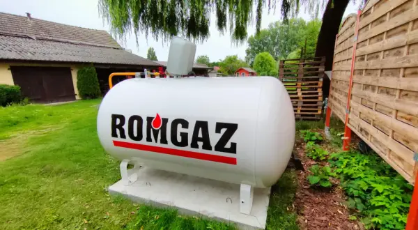 Biały zbiornik na gaz ziemny z napisem ROMGAZ, podłączony do instalacji ogrzewania gazowego z butli.