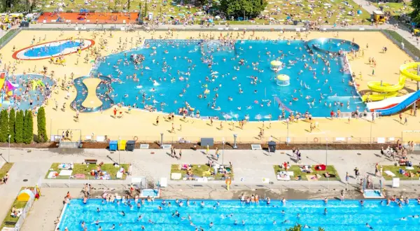 Tłum ludzi cieszy się słońcem i wodą w moczydło water park. W basenach i na trawie panuje wakacyjna atmosfera.