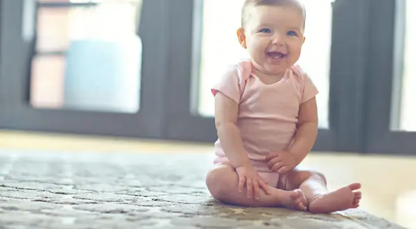 Ein fröhliches Baby sitzt auf einem Teppich und lacht.