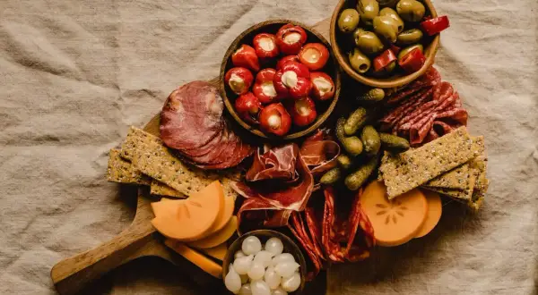 Tabla de que es charcuteria: embutidos, aceitunas, pepinillos, pimientos rellenos, queso y galletas.