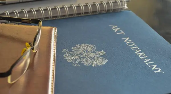 Akt notarialny z orłem, obok notes i okulary. To ważne dokumenty, tworzące repertorium prawnicze.