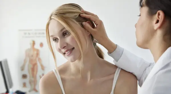 Lekarz bada skórę głowy pacjentki. Czy potrzebuje skierowania do dermatologa?