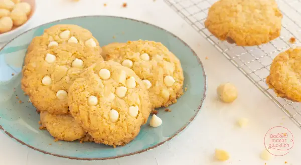 Saftige white chocolate macadamia cookies auf einem türkisfarbenen Teller, daneben Macadamianüsse und Schokostückchen.