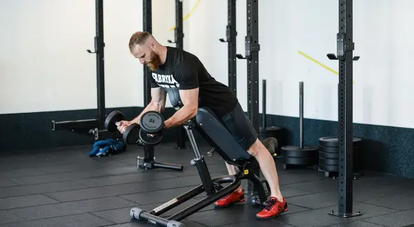 Mężczyzna wykonuje ćwiczenie incline dumbbell curl na ławce skośnej, budując masę mięśniową ramion.