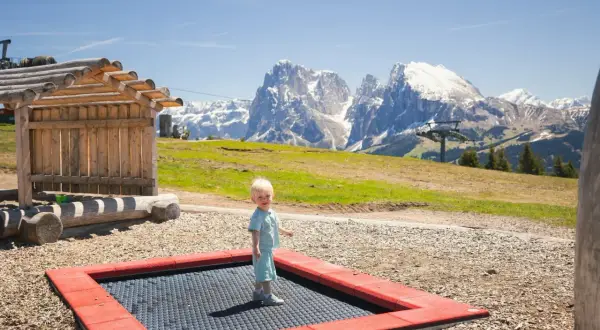 Mały chłopiec cieszy się zabawą na trampolinie na tle majestatycznych Dolomitów.
