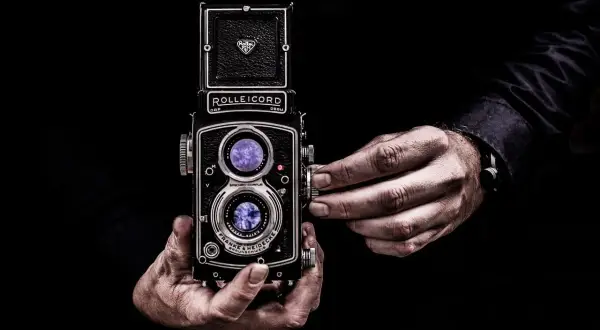 Dłonie trzymające aparat Rolleicord, uchwycone w kadrze zgodnym ze złotym podziałem.