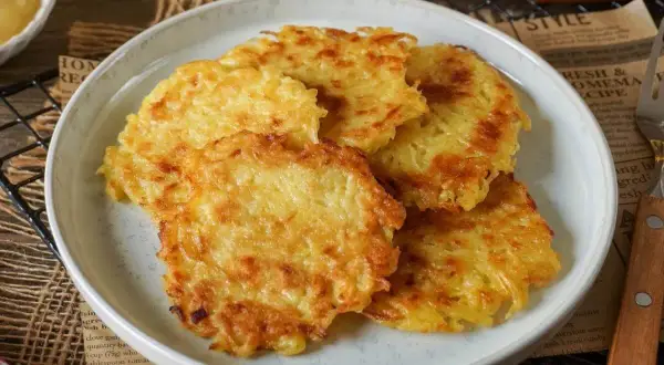 Goldbraune, knusprige Kartoffelpuffer aus gekochten Kartoffeln liegen auf einem Teller. Dazu passt Apfelmus.
