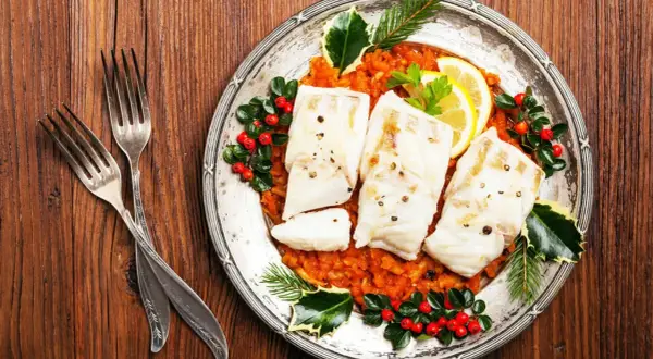 Gedünsteter Fisch auf Tomatenragout, festlich dekoriert mit Beeren und Tannenzweigen. Ein Gericht, das an italienische Weihnachtsrezepte erinnert.