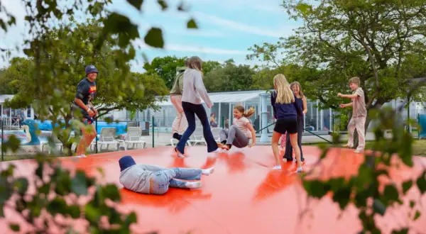 Barn hoppar på en stor orange studsmatta vid first camp råå vallar-helsingborg. Solen skiner och det är en härlig sommardag.