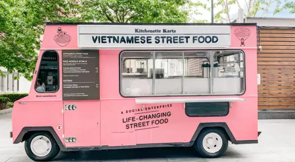 Un food truck rosa brillante, "Kitchenette Karts", offre "Vietnamese Street Food" e cibo che cambia la vita.