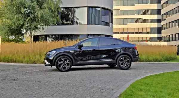 Elegancki, czarny Renault Arkana na tle nowoczesnych budynków biurowych.