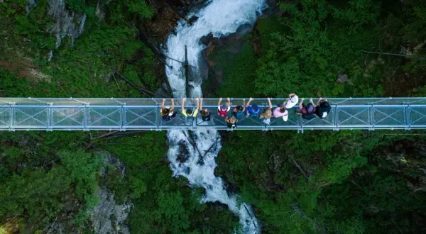 Un gruppo di persone ammira la cascata nel **Val di Rabbi** da un ponte sospeso.