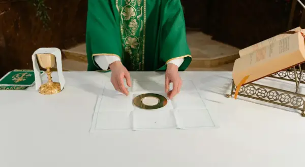 Kapłan przygotowuje się do udzielenia komunii. Na ołtarzu kielich, patena z hostią i księga.