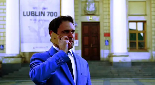 Mężczyzna w garniturze rozmawia przez telefon przed budynkiem z napisem "Lublin 700". Czy adwokat z urzędu jest płatny?