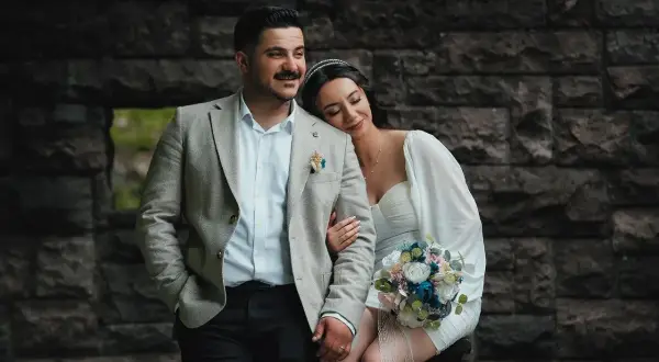 Para młoda w dniu ślubu, ona opiera głowę na jego ramieniu, trzyma bukiet.