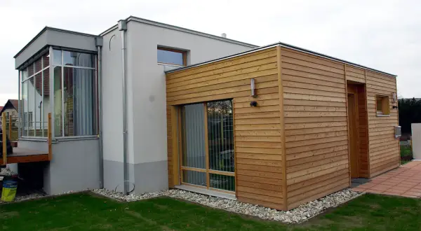 Moderner Anbau an altes Haus: Ein Teil des Hauses ist mit Holz verkleidet, der andere Teil verputzt. Große Fensterfronten und ein Wintergarten.
