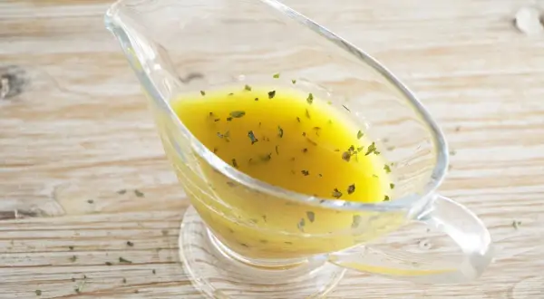 Salsa dorada con hierbas verdes en una salsera de cristal. Perfecta vinagreta de mostaza para realzar tus platos.