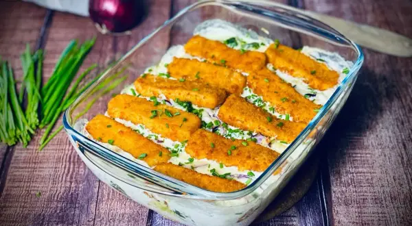 Ausgefallene Gerichte: Fischstäbchen-Auflauf mit cremiger Soße und frischen Kräutern, garniert mit Schnittlauch.