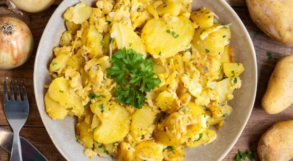Herzhafte bratkartoffeln mit ei, garniert mit Petersilie. Dazu rohe Kartoffeln und Zwiebeln.
