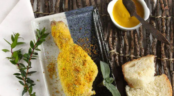 Fusi di pollo al forno dorati e croccanti, serviti con pane fresco, salsa gialla e rametti verdi.