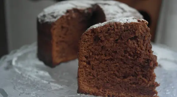 Un trozo de el mejor bizcocho de chocolate del mundo, espolvoreado con azúcar glas, sobre una bandeja de cristal.