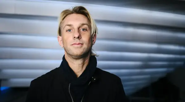 Anders Hansen, din personlighet speglas i blicken. En man med karisma, klädd i svart jacka och scarf, mot en bakgrund av horisontella linjer.