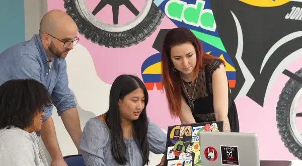 Apprendre comment devenir un développeur web avec des collègues devant un mur coloré.