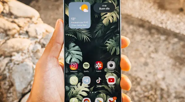Mano sujetando un teléfono Android con iconos de aplicaciones personalizables, mostrando cómo cambiar tamaño iconos android para una mejor visualización.