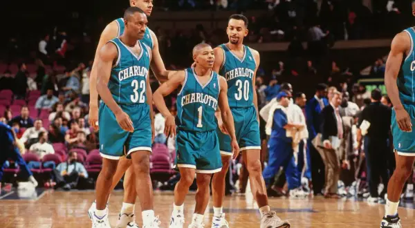 Koszykarze Charlotte Hornets, w tym najniższy koszykarz NBA, w turkusowych strojach na boisku.