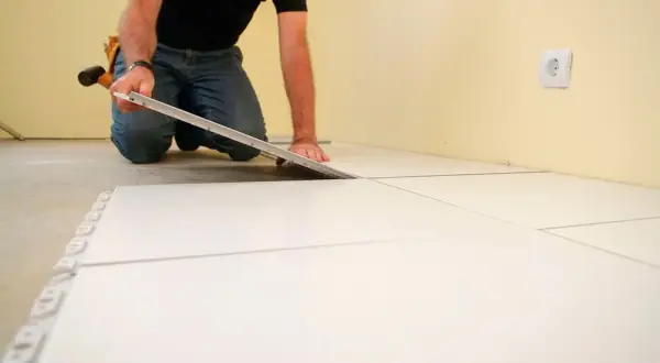 Hombre colocando baldosas blancas, un paso clave para como poner suelo porcelanico.