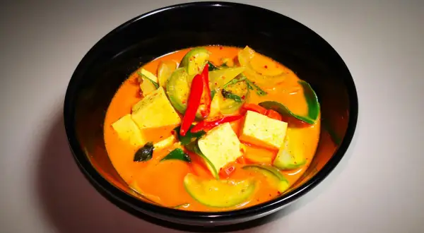 Ein dampfendes rotes Curry mit Tofuwürfeln, grünen Tomaten und scharfen Chilischoten. Dieses rote Curry ist scharf und verlockend.