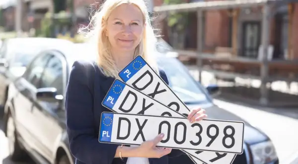 Kobieta trzyma tablice rejestracyjne z oznaczeniem DX. Nowe tablice dla Twojego auta, szybka dx rejestracja.