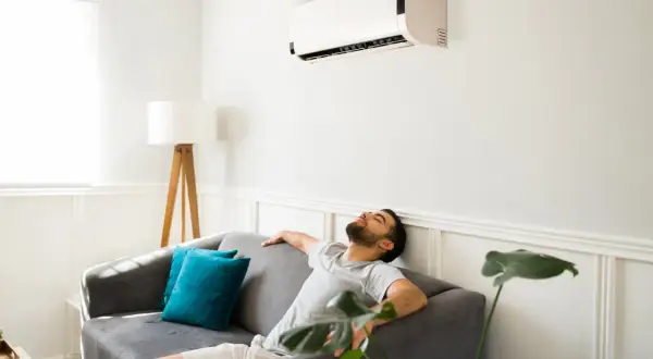 Un homme se repose sur un canapé sous la climatisation, ignorant les effets néfastes de la climatisation sur la santé et l'environnement.