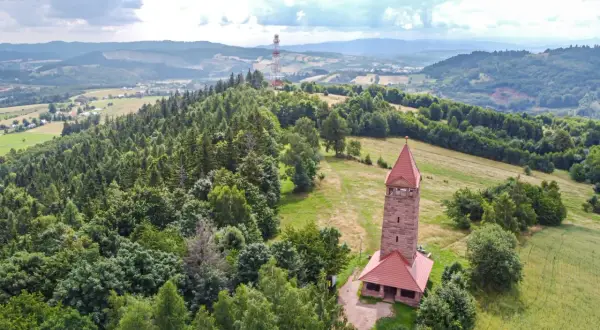 Kamienna wieża widokowa na wzgórzu, otoczona lasem i polami, oferuje wspaniałe widoki na krajobraz Dolnego Śląska.