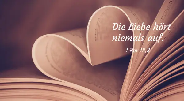 Ein aufgeschlagenes Buch formt ein Herz. Darauf steht: "Die Liebe hört niemals auf. 1 Kor 13,8". Bibelzitate über Liebe und Ehe.