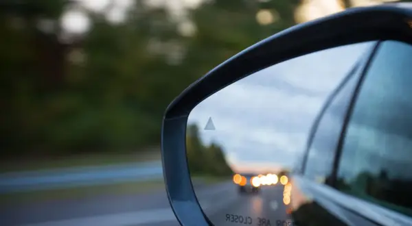 Specchietto retrovisore con indicatore del sistema side assist attivo, riflette la strada e le luci delle auto.