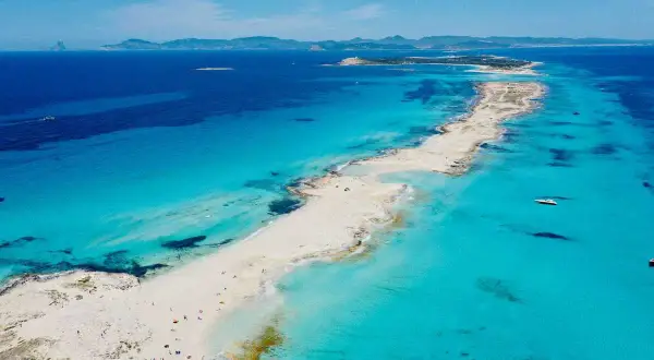 Arena blanca y aguas turquesas en la mejor playa de Formentera. Un paraíso con barcos y gente disfrutando del sol.