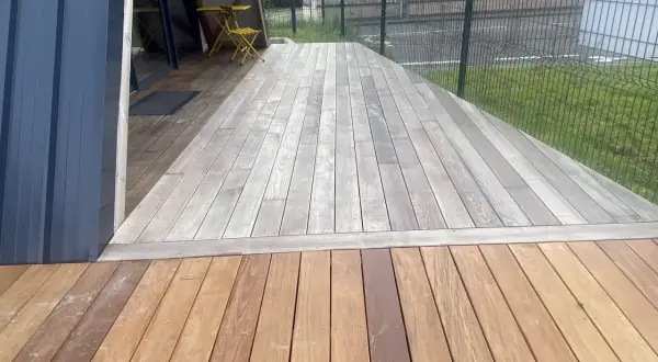 Terrasse en bois avec une partie grise, signe qu'il faut enlever le saturateur bois. Une table et une chaise jaunes sont visibles.