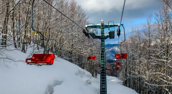 Seggiovia rossa su piste innevate ad Abetone, l'altitudine offre panorami mozzafiato tra alberi spogli coperti di neve.