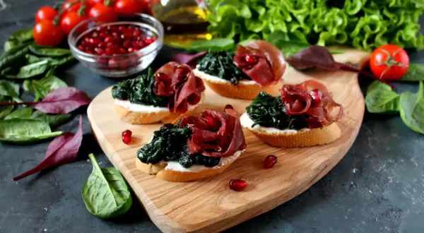 Leckere Bruschetta mit Spinat, Schinken und Granatapfelkernen – eine tolle Kombination eisenhaltiger Lebensmittel.