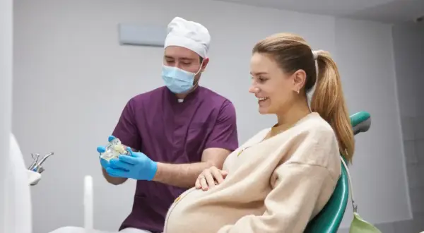 Dentysta wyjaśnia ciężarnej pacjentce procedurę leczenia kanałowego, pokazując model zębów.